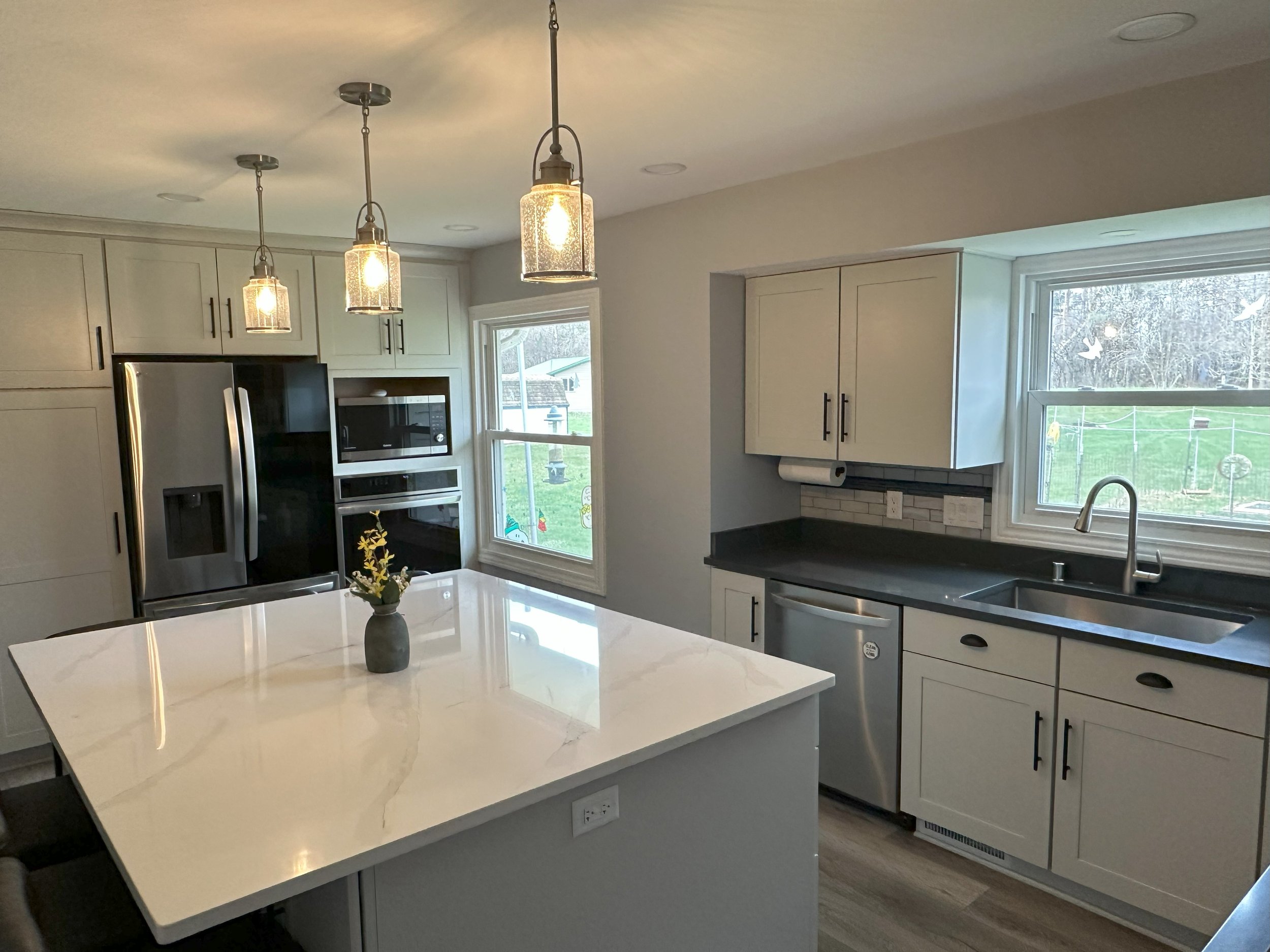 Modern kitchen with white cabinets, stainless steel appliances, and a large island with a vase and pendant lighting.