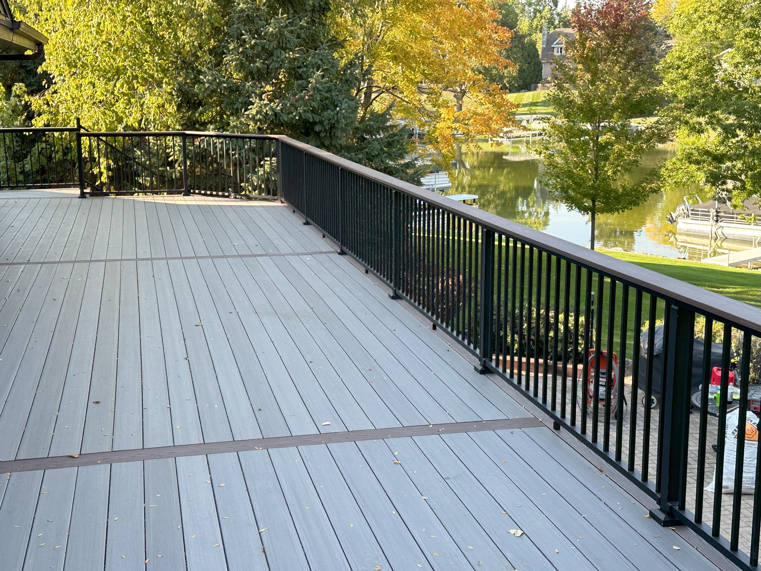 Large wooden deck with black metal railing overlooking a pond and trees with autumn foliage.