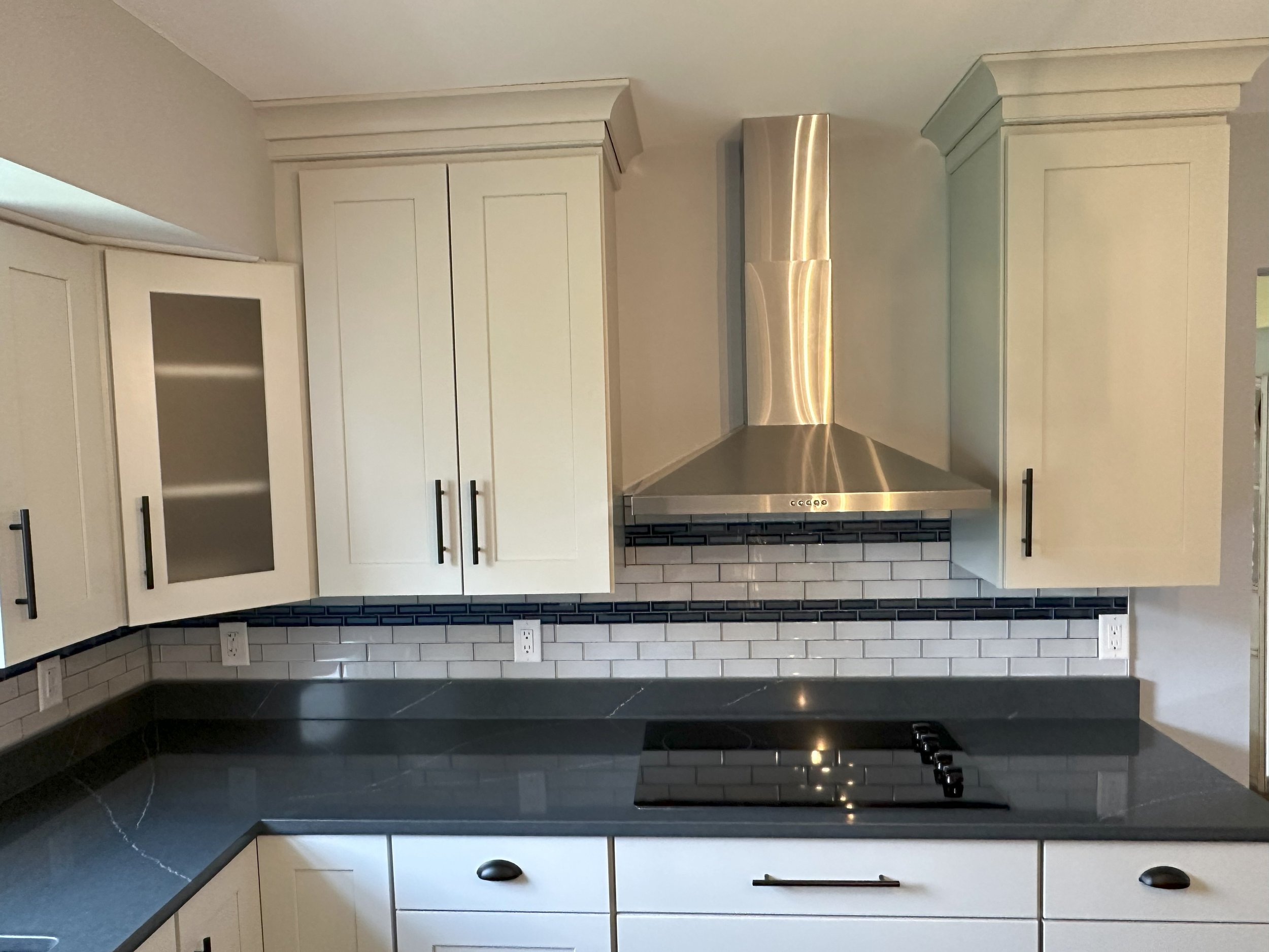Modern kitchen with white cabinetry, stainless steel range hood, black countertop, and subway tile backsplash.
