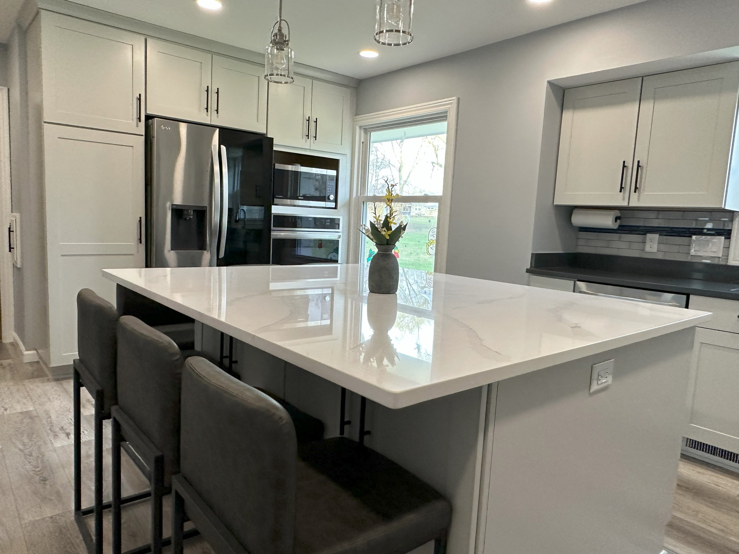 Modern kitchen with white cabinets, stainless steel appliances, large marble island, three bar stools, and pendant lights.