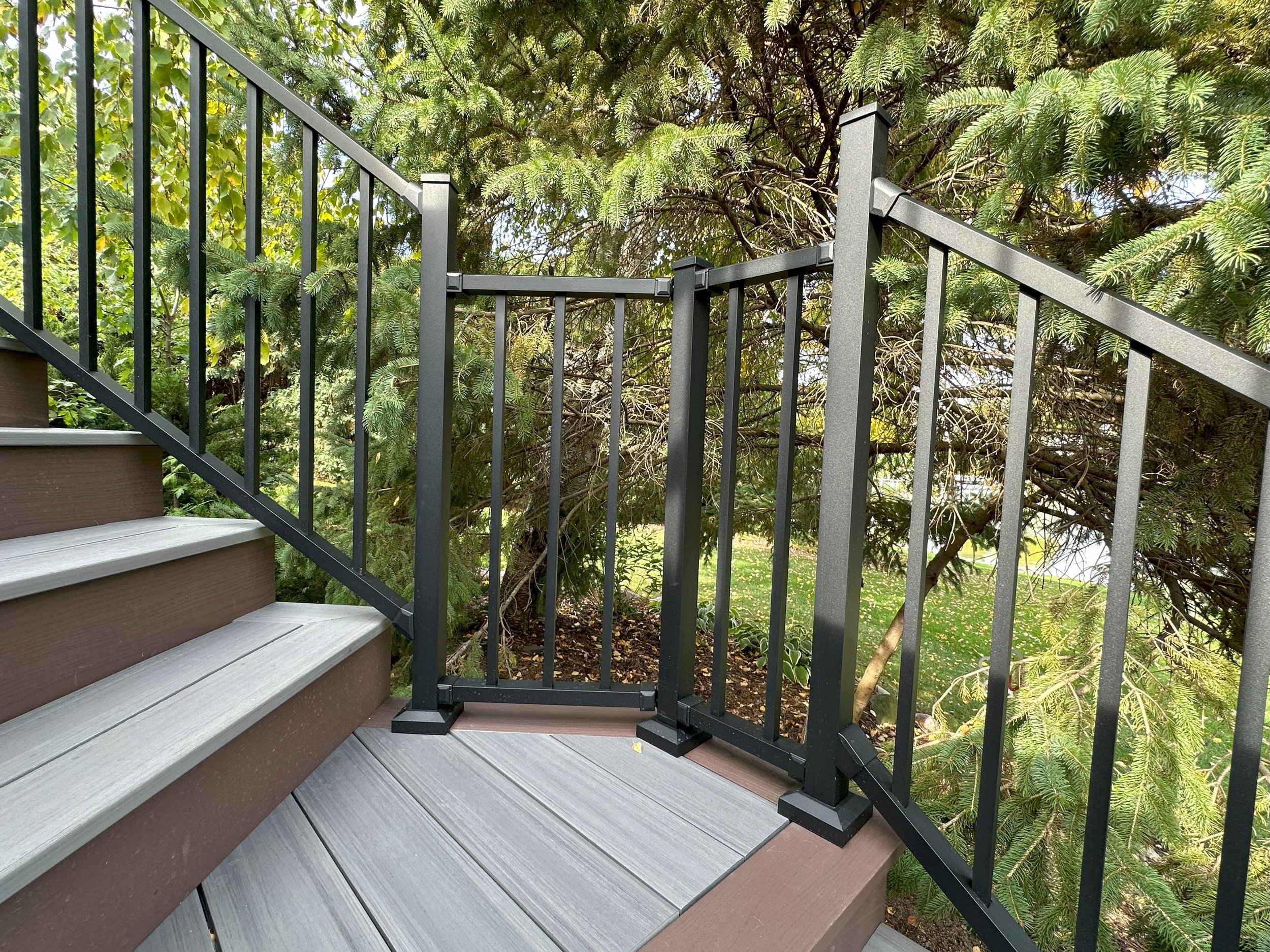 Outdoor deck with metal railing and stairs, surrounded by green trees and foliage.