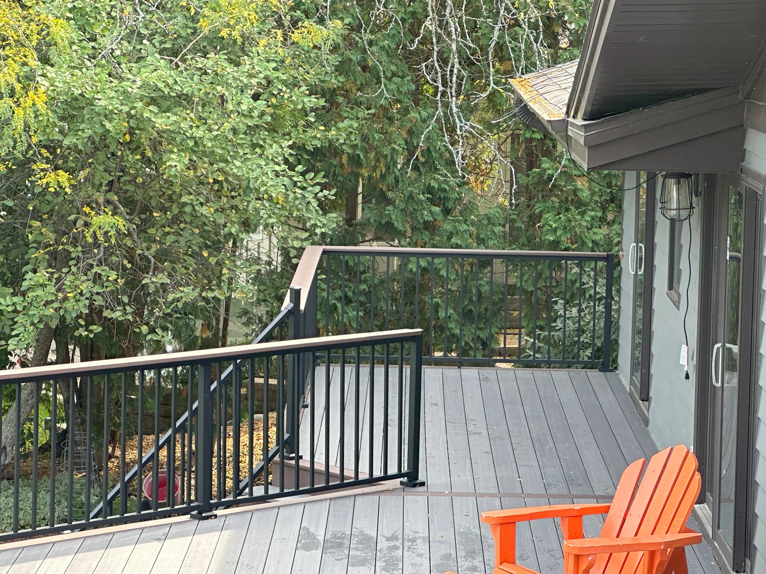 Wooden deck with black railing, orange Adirondack chair, trees in background