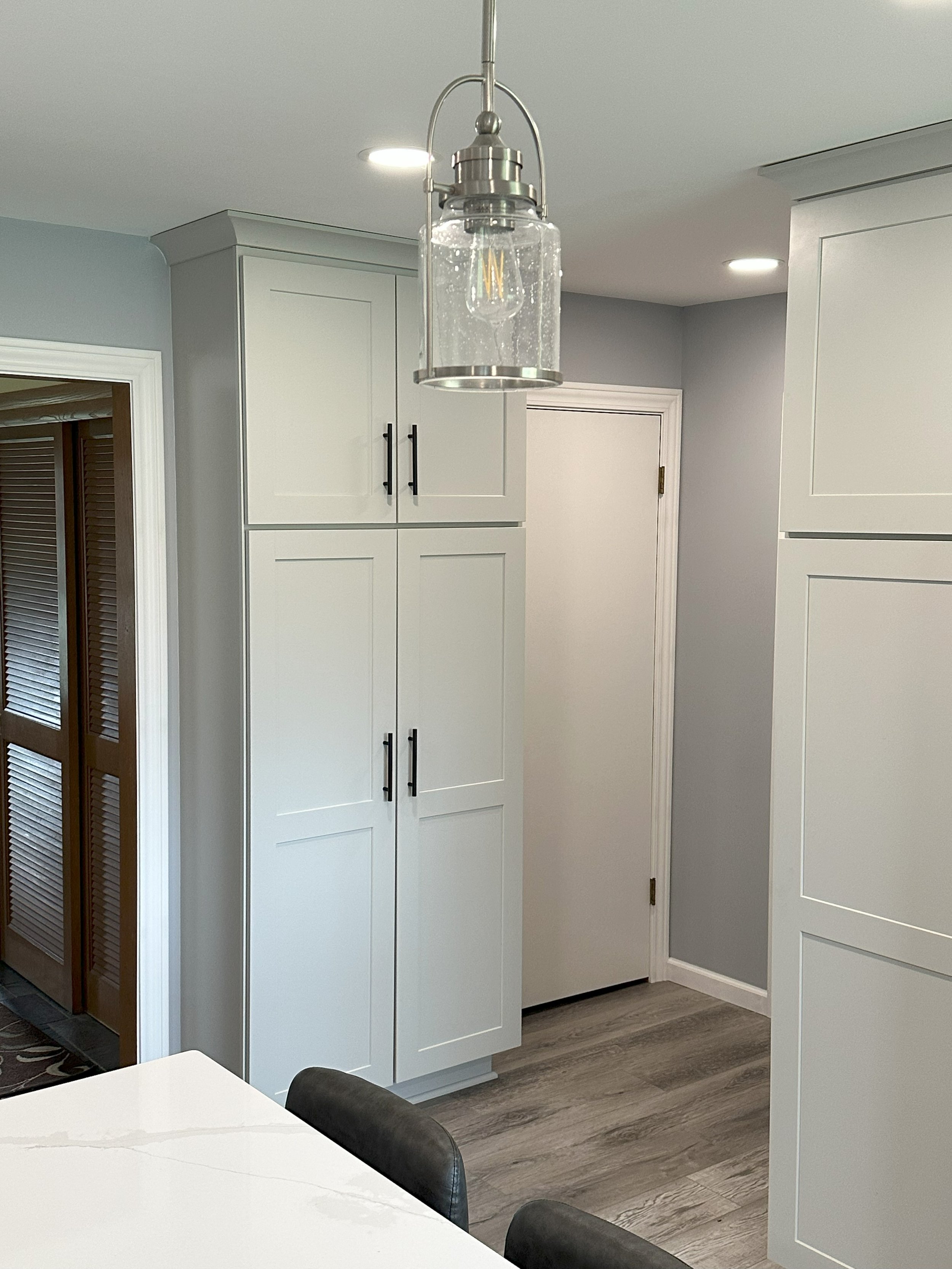 Modern kitchen interior with gray walls, white cabinets, pendant light, and light wood flooring.