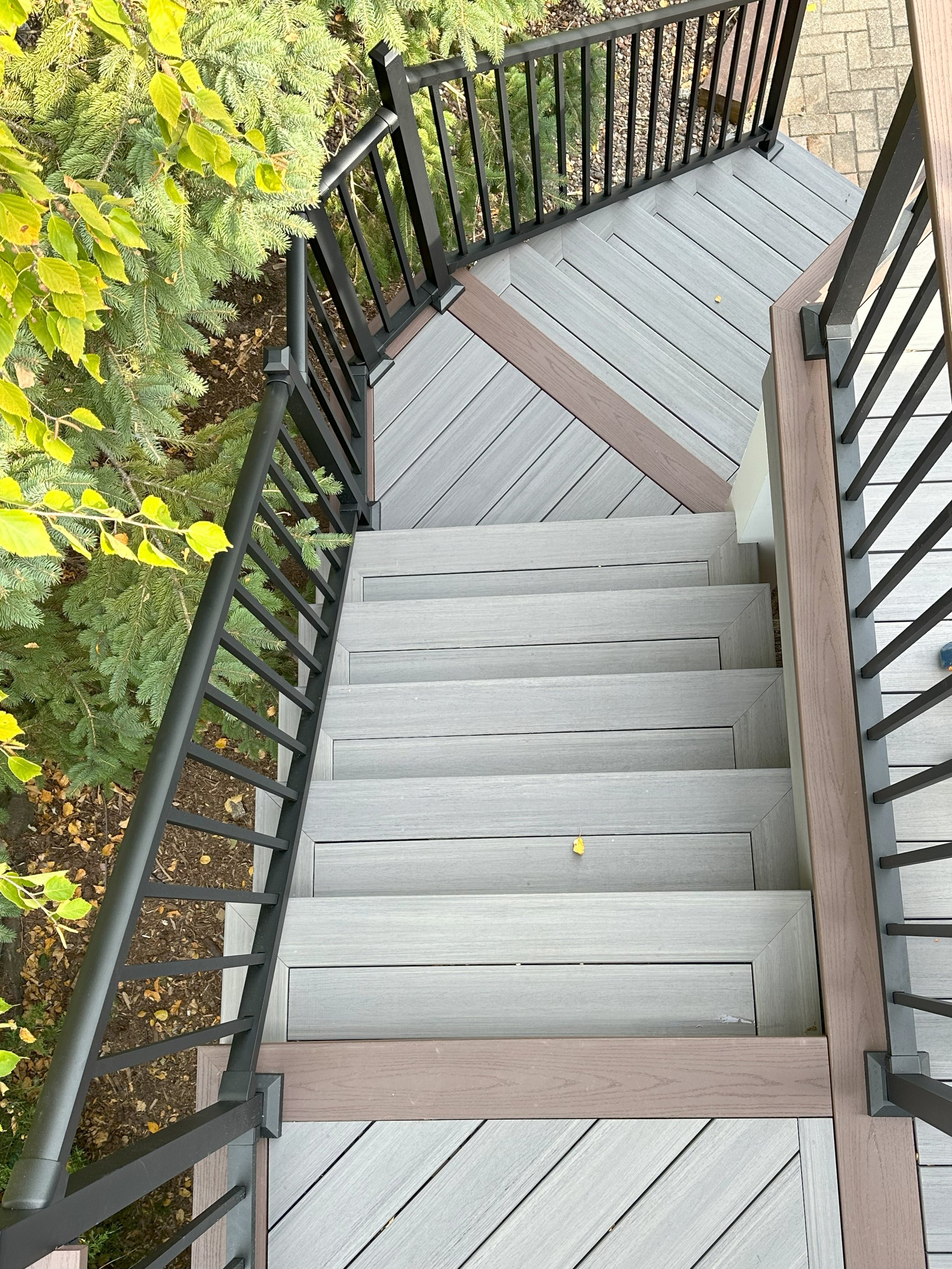 Top view of outdoor wooden stairs with black railings, surrounded by green foliage.