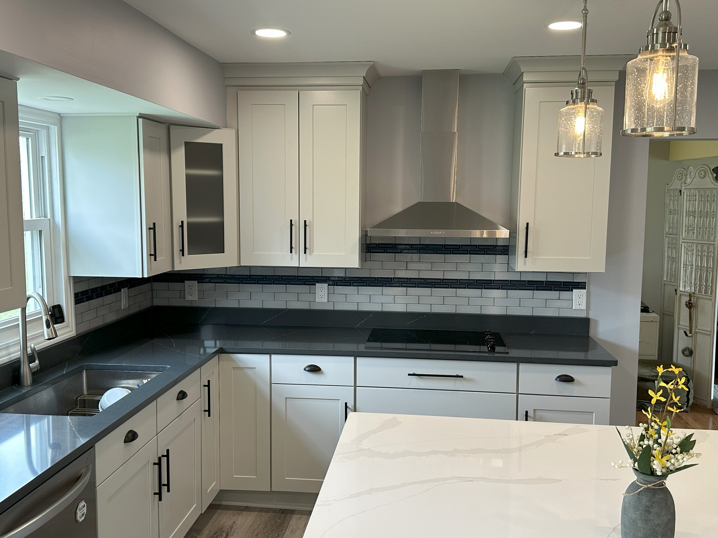 Modern kitchen with white cabinets, a stainless steel range hood, black countertops, pendant lighting, and a vase with flowers on the island.
