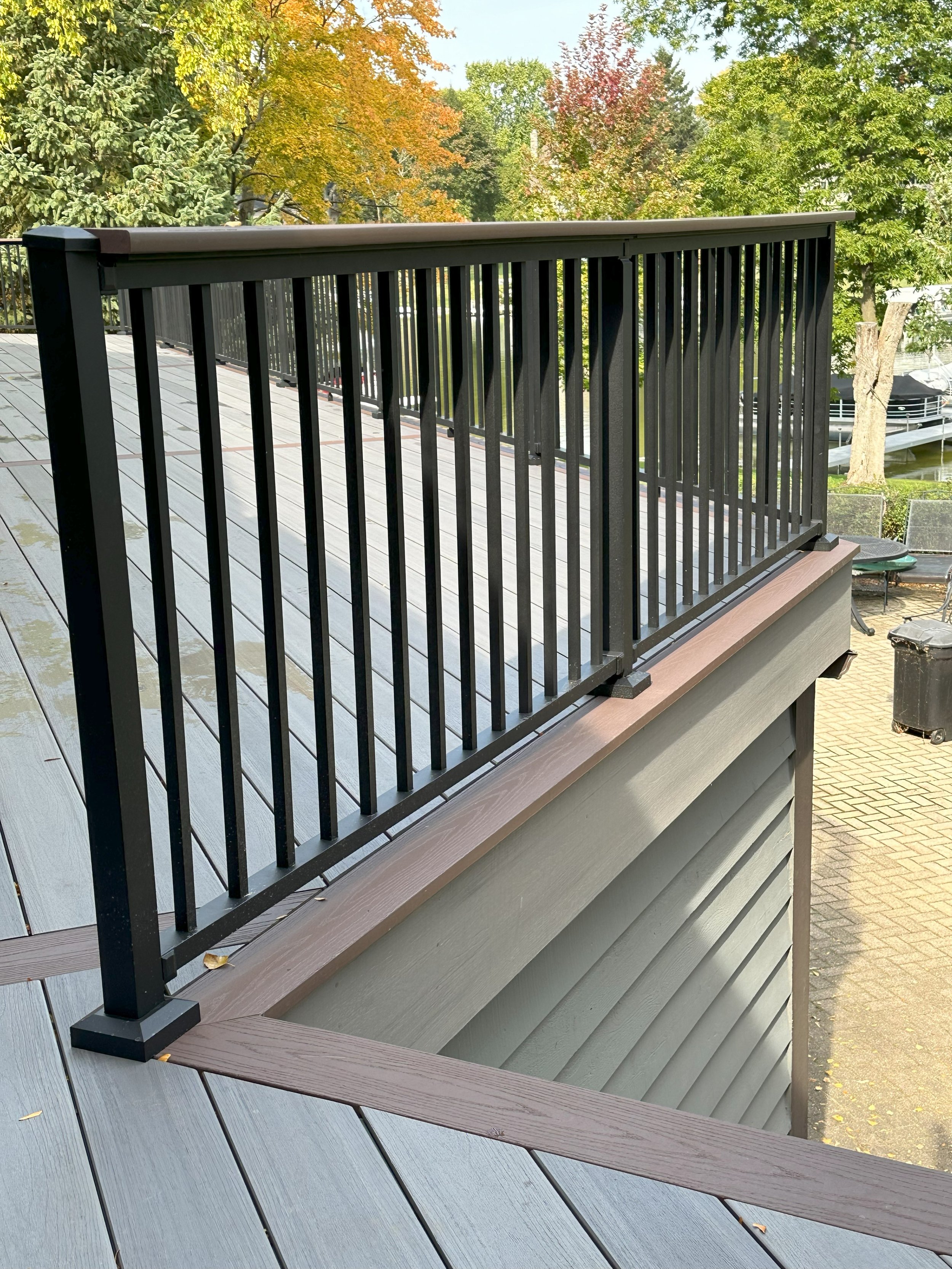View of a patio deck with black metal railings and a sloping roof, surrounded by trees with autumn foliage.