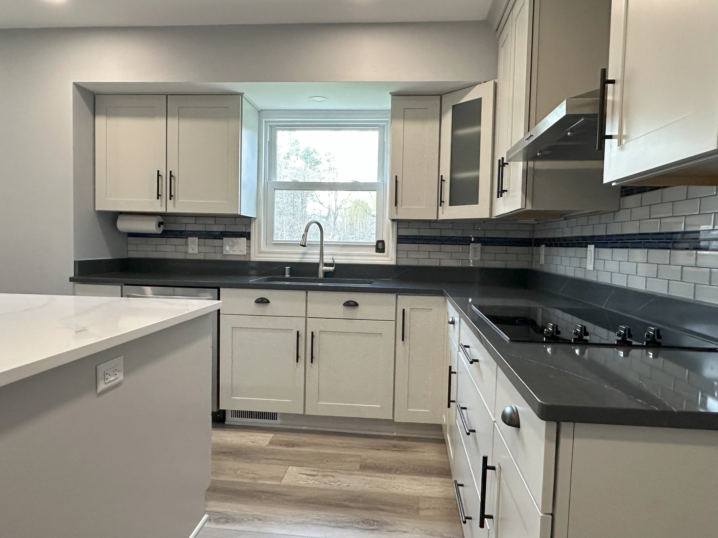 Modern kitchen with white cabinets, black handles, gray countertops, glass tile backsplash, a window above the sink, and an electric cooktop.