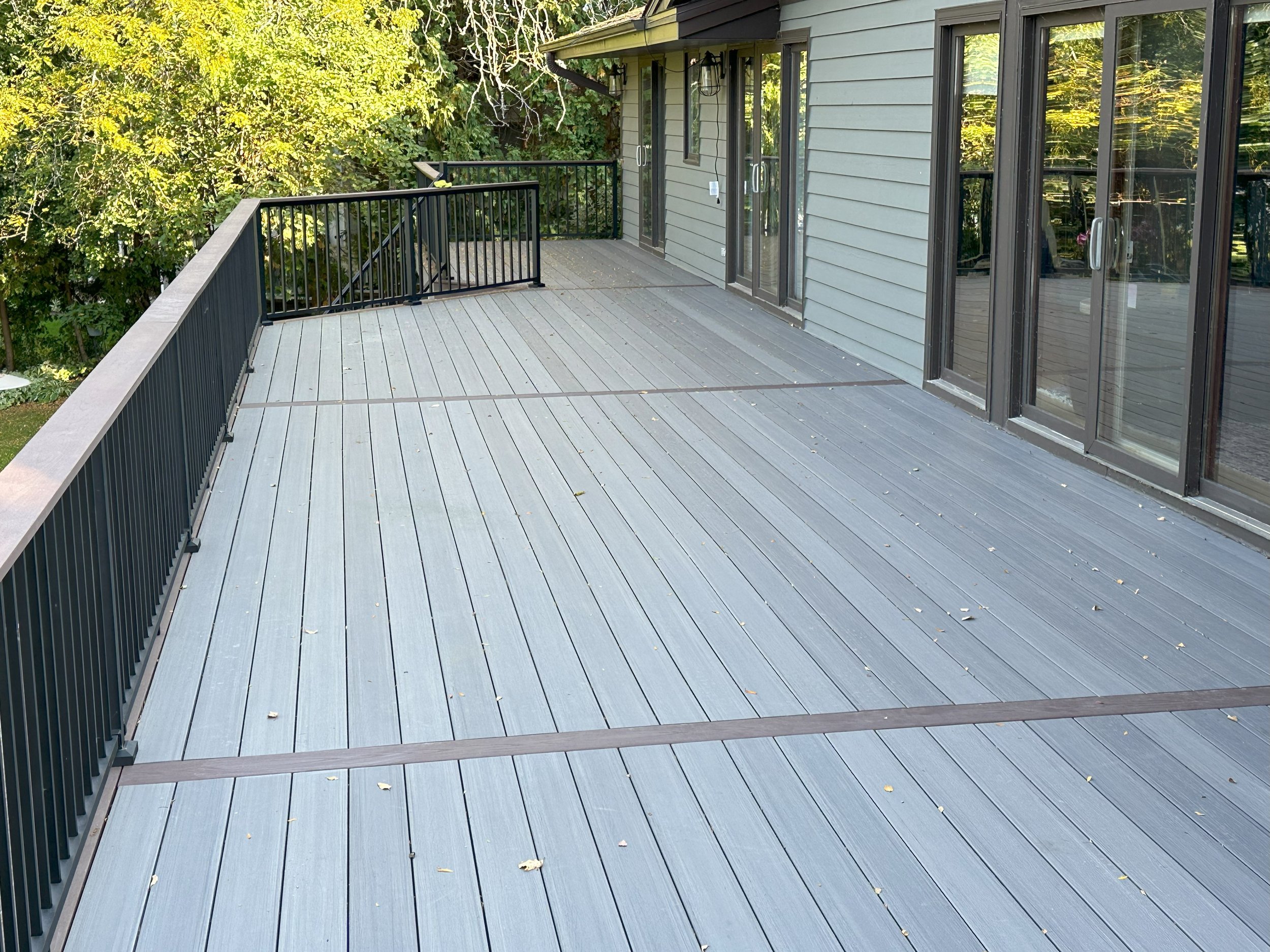 Spacious outdoor deck with gray composite flooring and black metal railing attached to a house with large sliding glass doors.