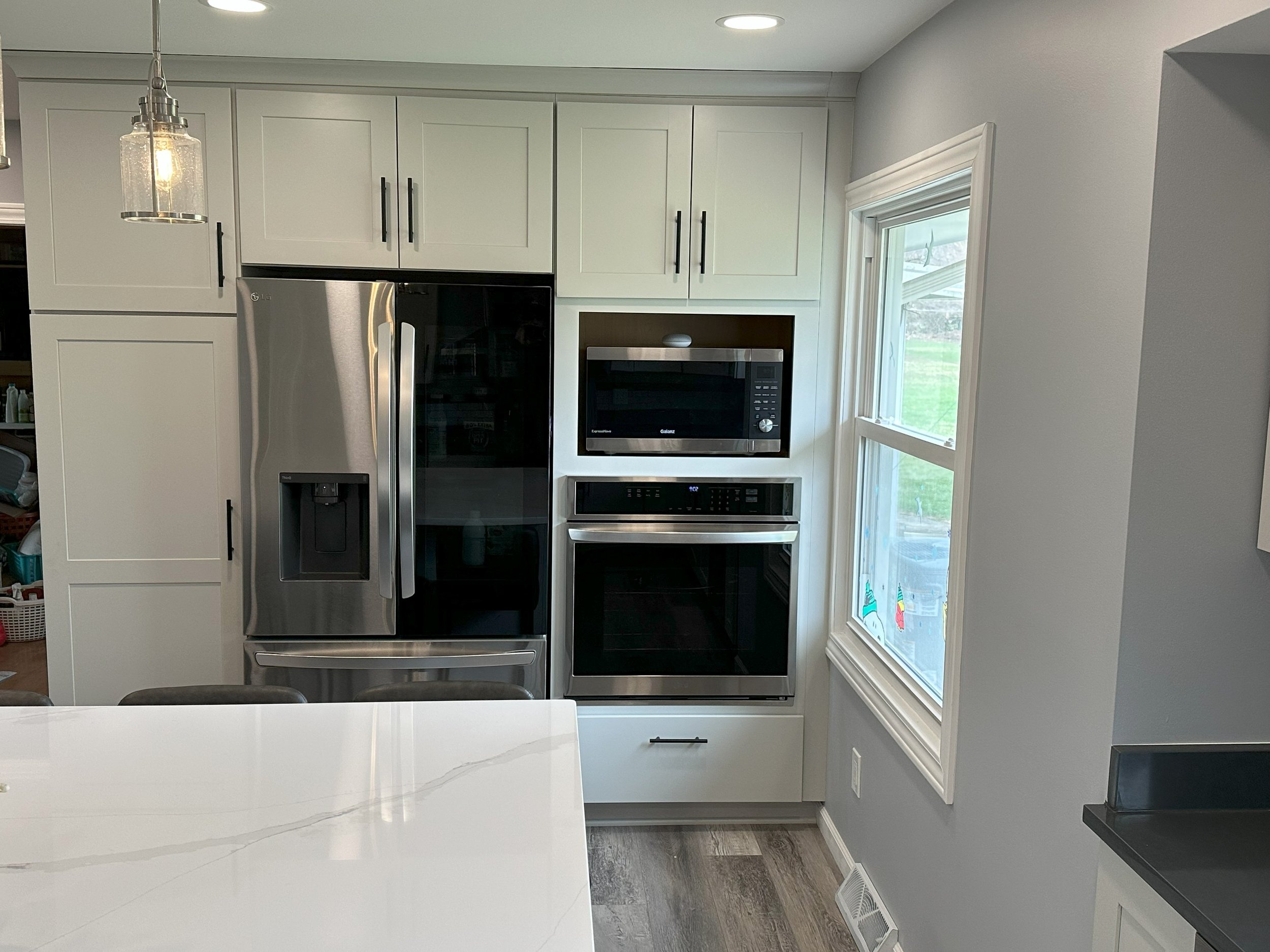 Modern kitchen featuring stainless steel refrigerator, built-in microwave, and oven, with white cabinets and a marble countertop.