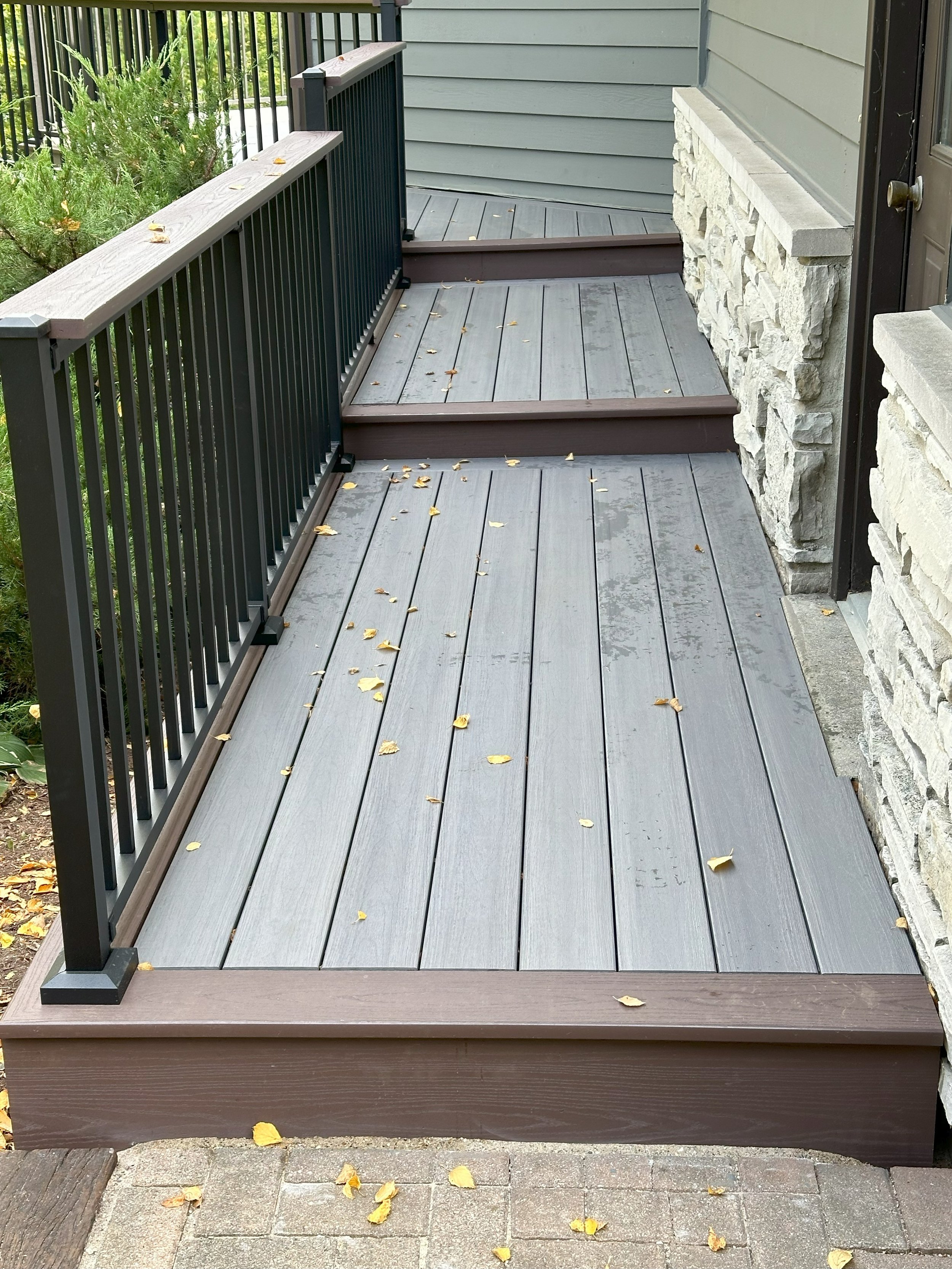Gray wooden ramp with metal railing next to a building with stone facade, scattered with yellow leaves.