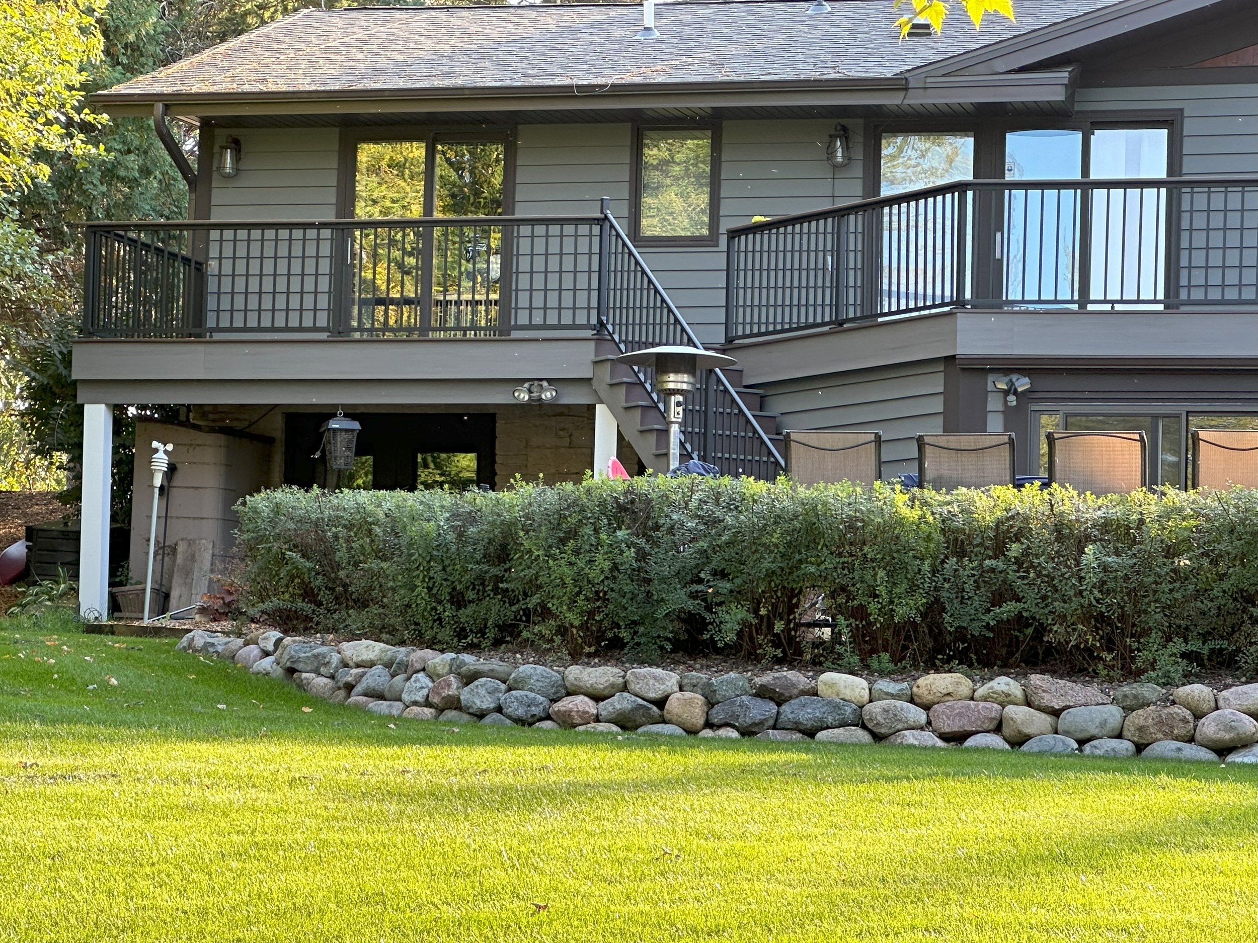 Suburban house with balcony, patio chairs, and landscaped garden with shrubs and stone border.