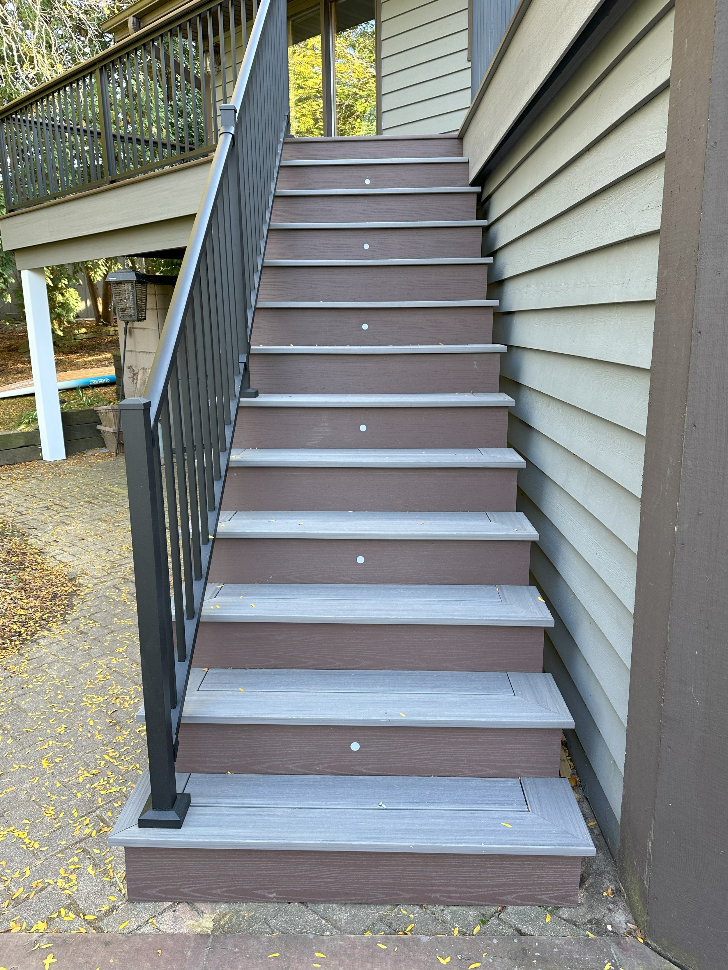 Outdoor wooden staircase with dark railing attached to a house, leading up to a porch area.