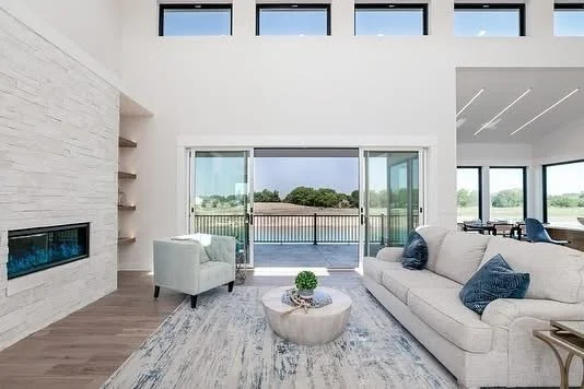 Modern living room with large sliding glass doors opening to a balcony and green outdoor scenery, featuring white and blue furniture.