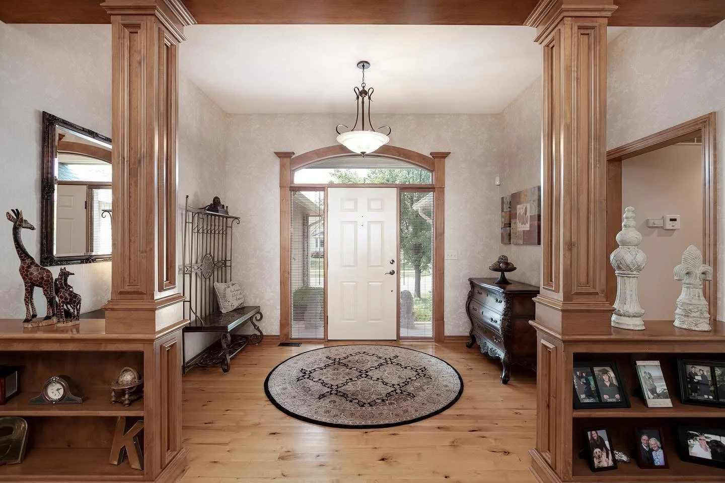Entryway of a house with a front door, hardwood floors, decorative wood trim, bench, side table, and framed photos.