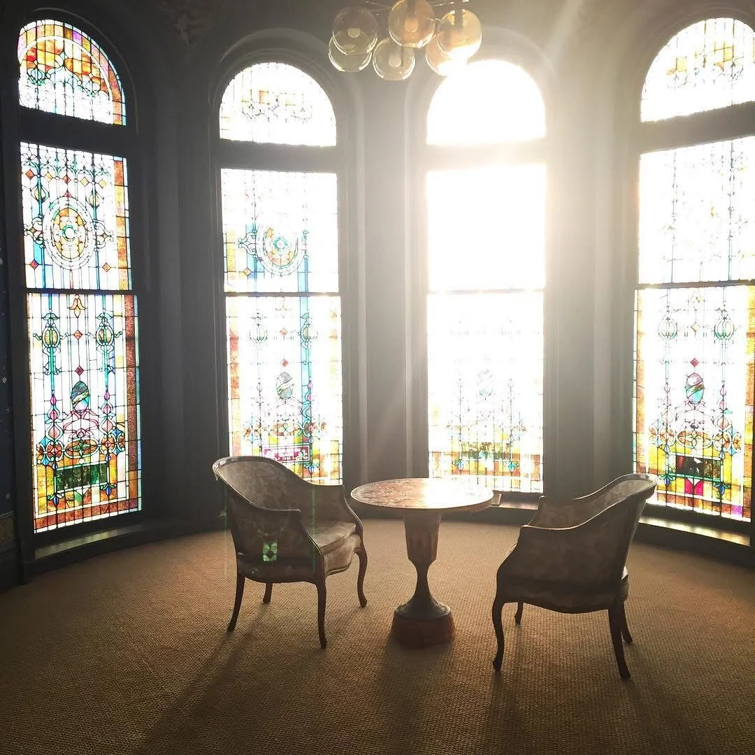 Vintage room with stained glass windows, a small round table, and two upholstered chairs with wooden legs.