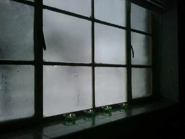 A window with multiple panes and black framing, with four small green candle holders on the windowsill.