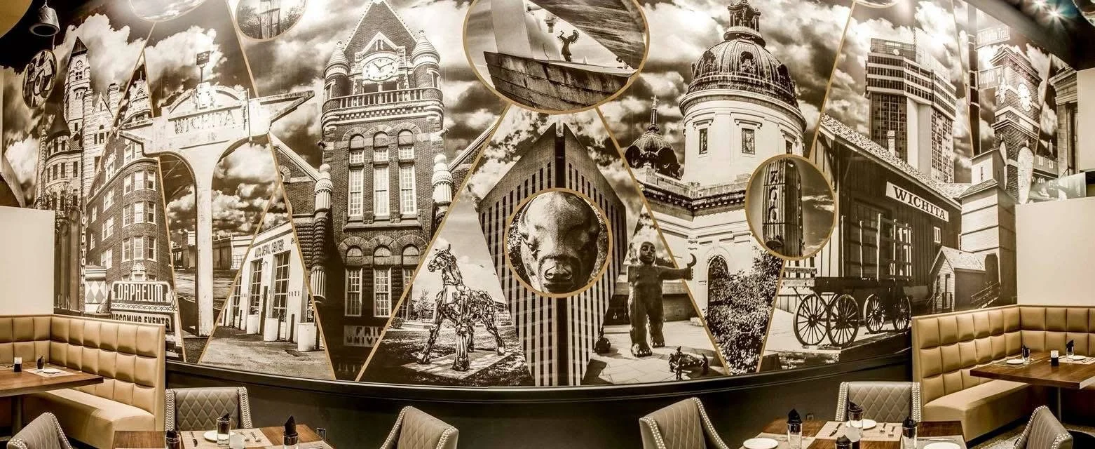Black and white collage mural of various historic and cultural landmarks of Wichita, Kansas, with seating areas and tables in the foreground.