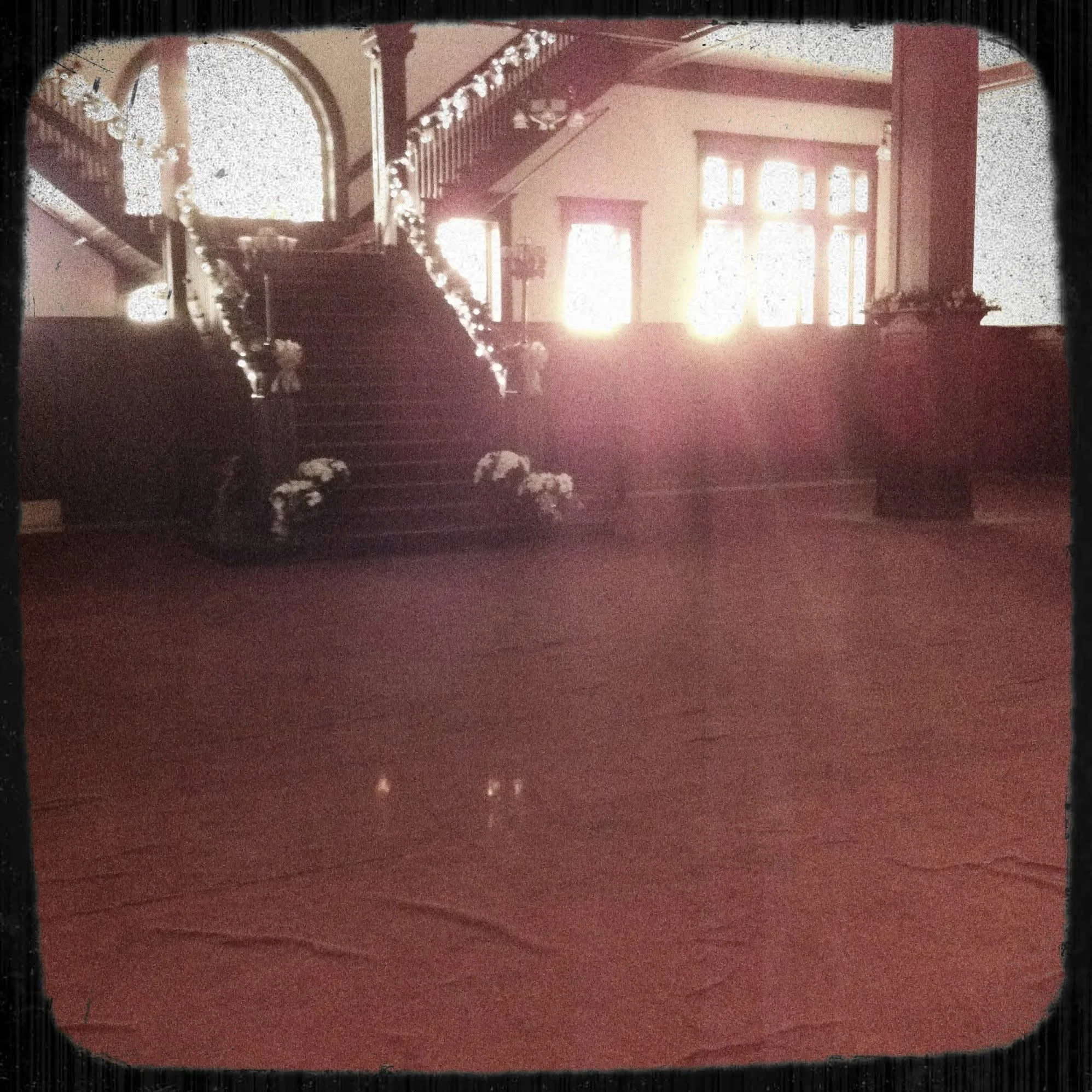 Interior of a church with a staircase decorated with garland and flowers, sunlight streaming through large windows.