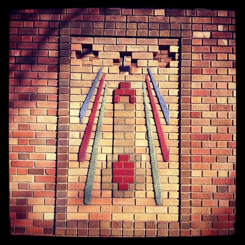 Brick wall with artistic relief of a cat's face and body, created with bricks of different colors and shapes.