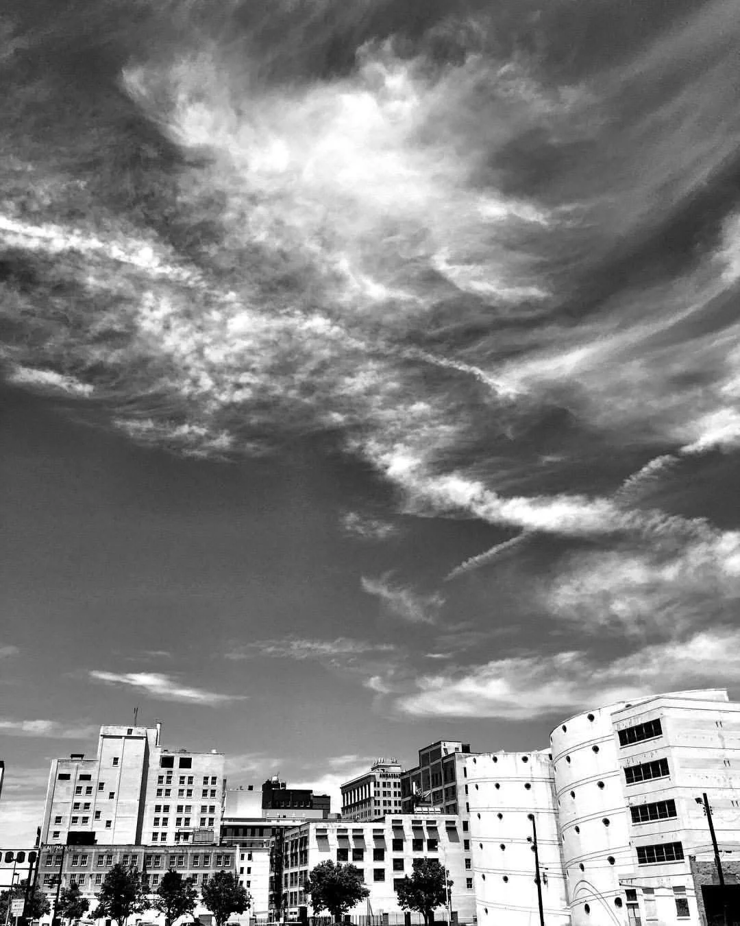 Black and white photo of city buildings and a partly cloudy sky.