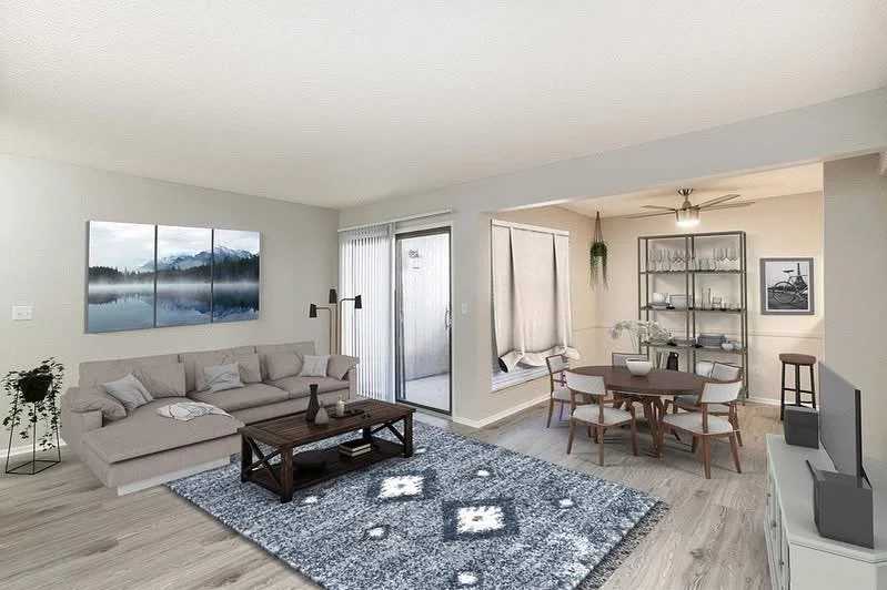 Living room with a beige sofa, wooden coffee table, blue patterned rug, and wall art; adjacent dining area with a round table and chairs, a glass shelf, and a window with curtains.