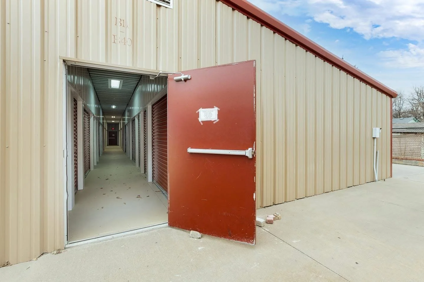 Exterior of a storage facility with an open door leading to a hallway of storage units.