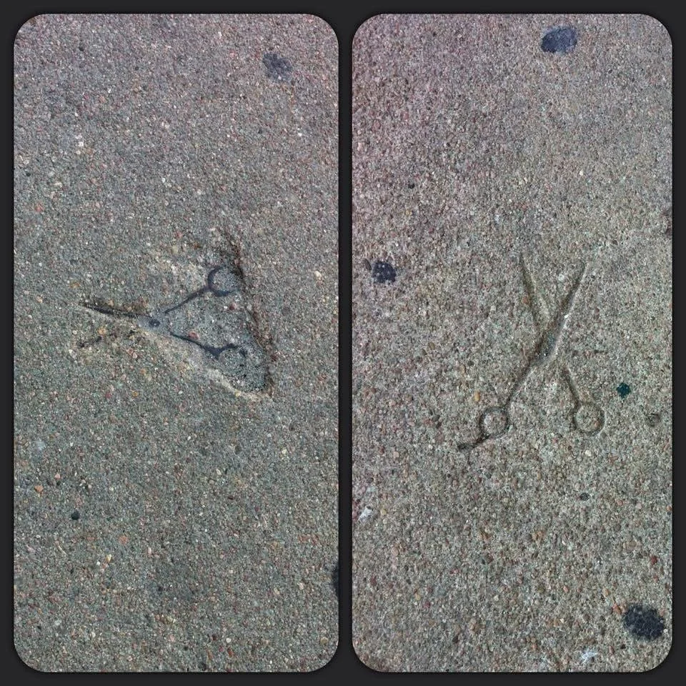 Footprints and a pair of small scissors drawn in sand, with the scissors crossed.