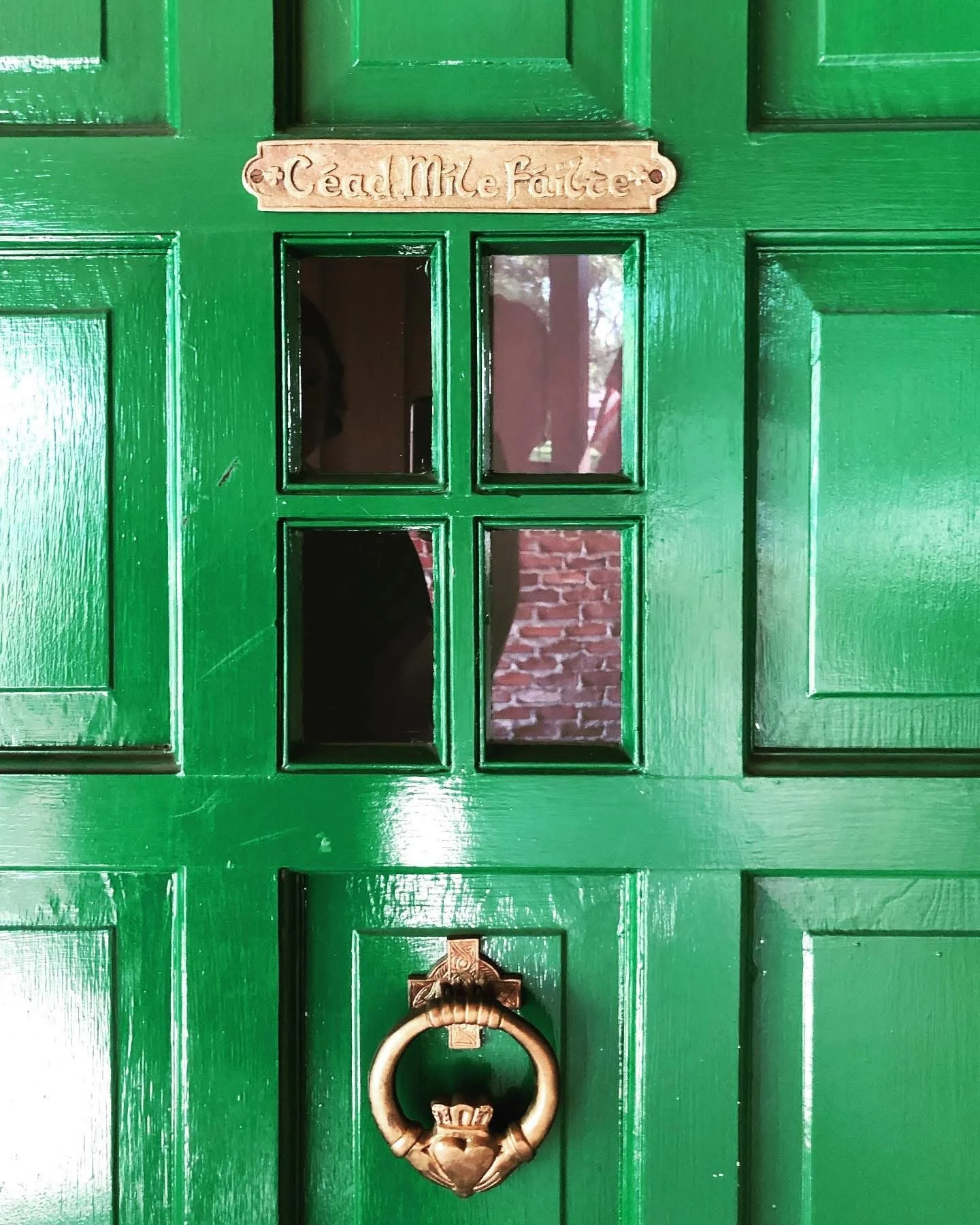 Close-up of a bright green wooden door with a brass knocker and a brass plaque above that reads 'Tea. Mile Faitree'.