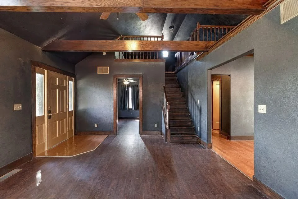 Interior of a house with dark walls, wooden doors, a staircase, and a loft area with wooden railing.
