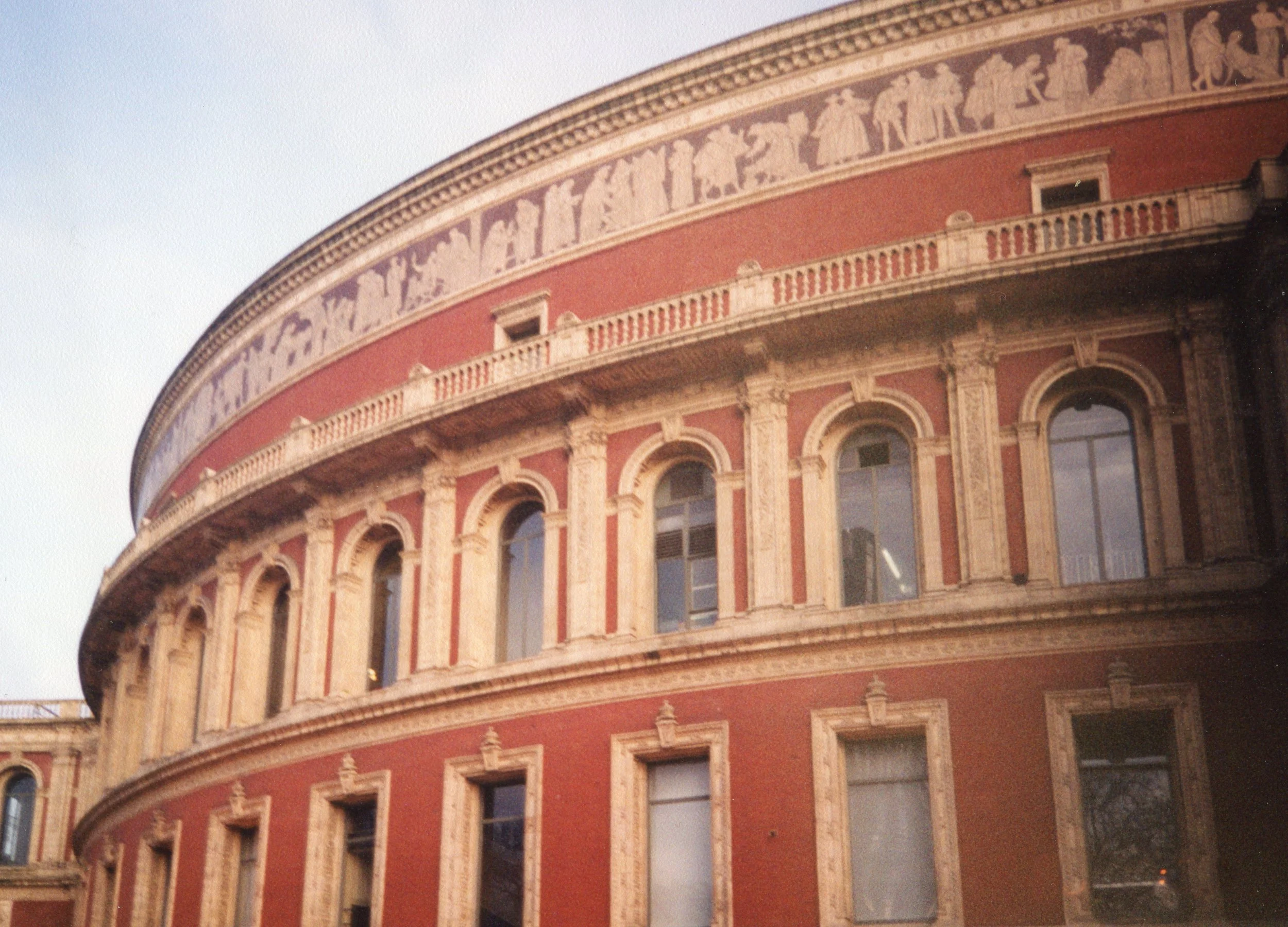 A round, historic building with red walls and ornate stone detailing, featuring several arched windows.
