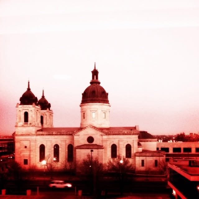 A historic church with two towers and a central dome, set against a light sky at dusk.