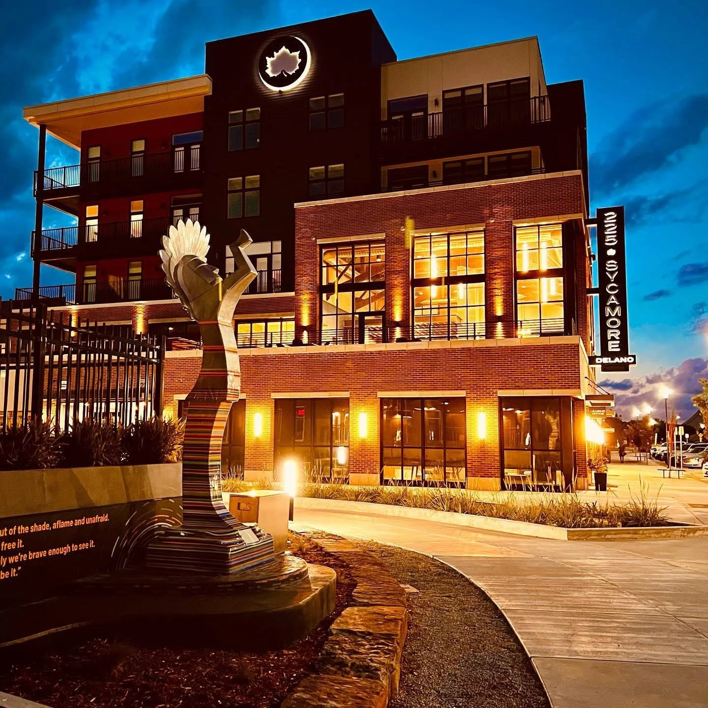 Nighttime view of a multi-story brick building with lit windows, a sign that reads 'Yosemite' and an abstract sculpture in the foreground.