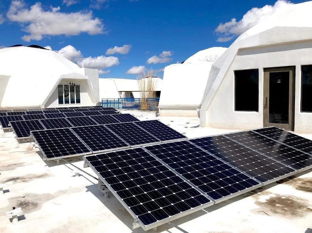 Solar panels installed on a flat rooftop of a building with white walls, under a blue sky with scattered clouds.