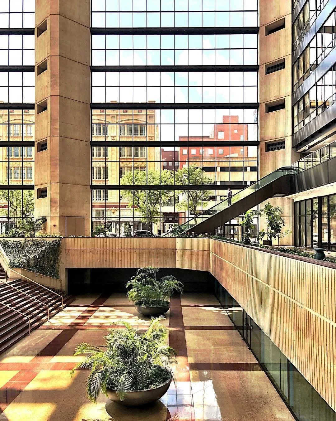 Interior view of a modern office building with large glass windows, indoor plants, and an escalator.