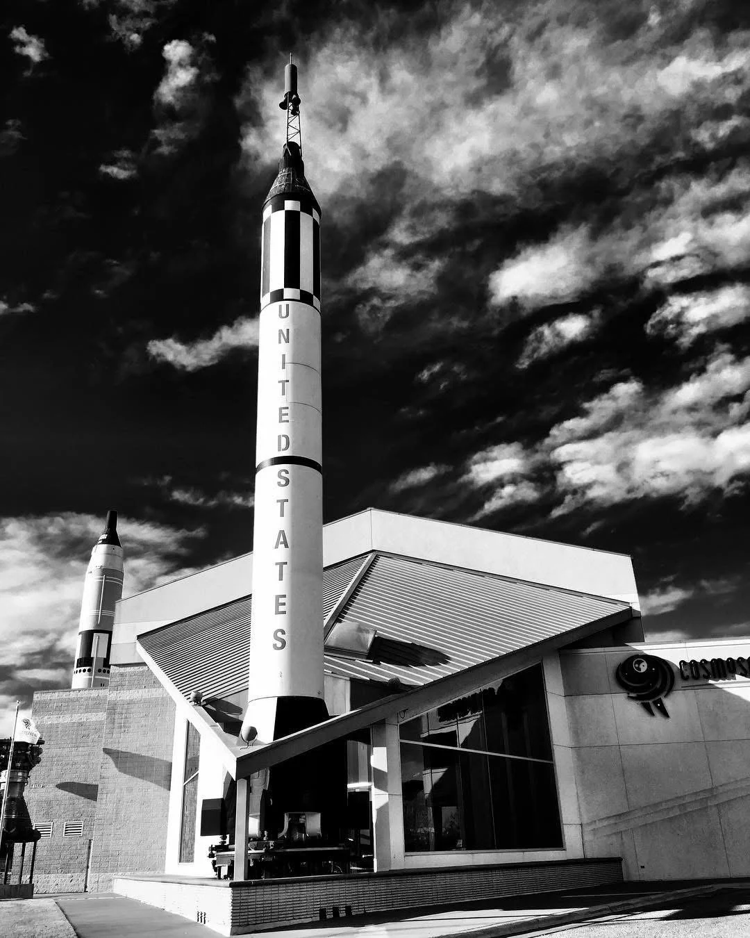Black and white photo of the Smithsonian National Air and Space Museum with rockets in front and a dramatic sky.