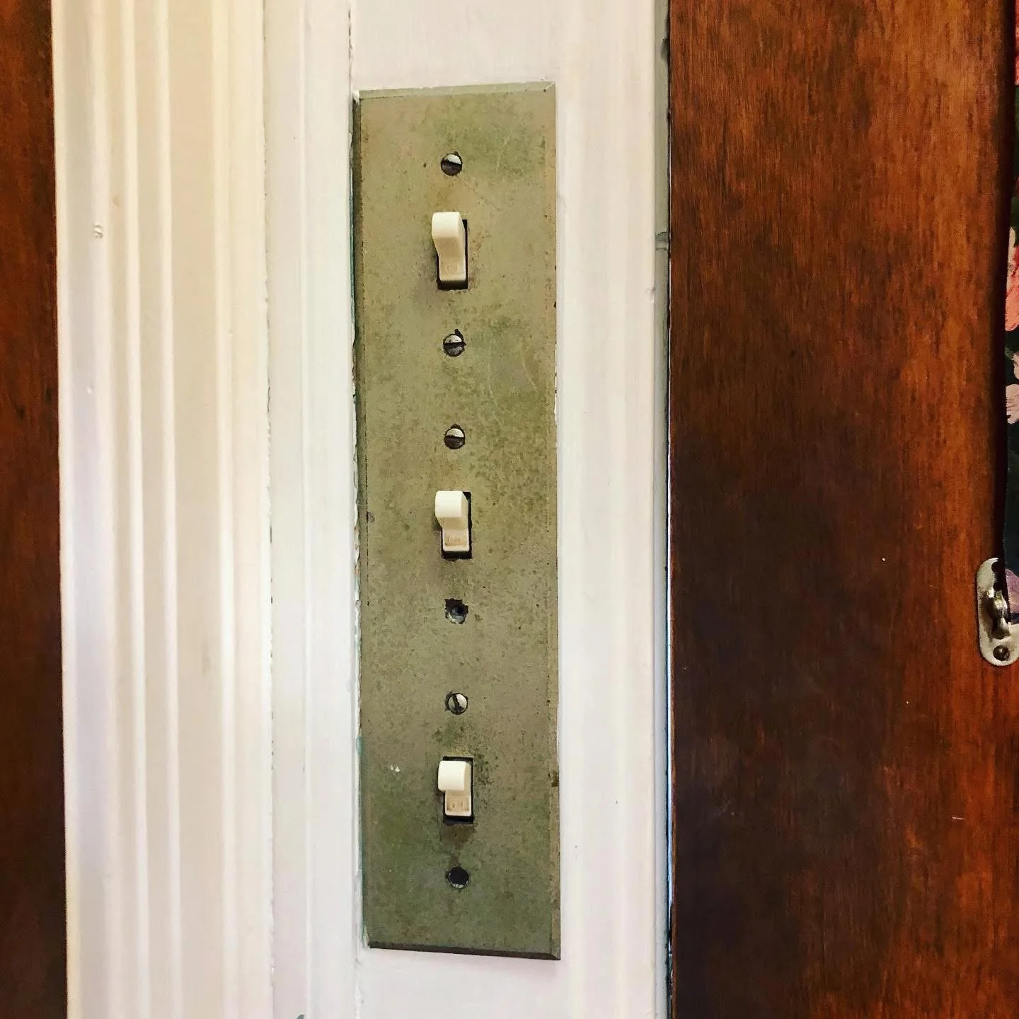 Close-up of an old, unused light switch panel with five switches on a wall between a white wall and a wooden door.
