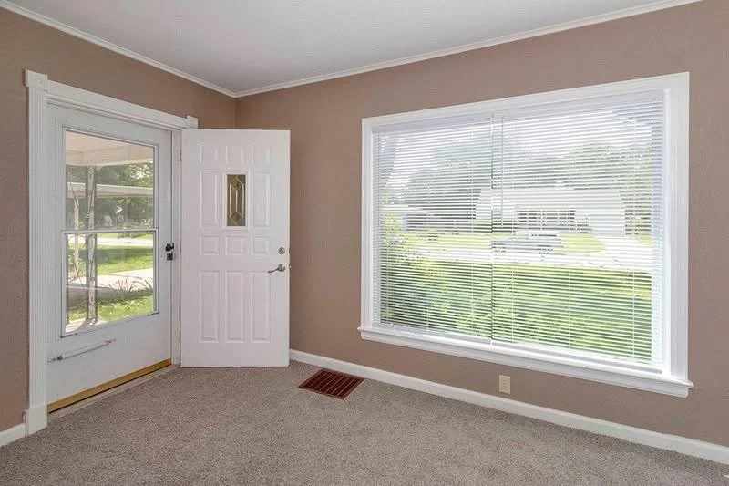 Interior of a room with a glass door and large window, beige walls, and gray carpeted floor.