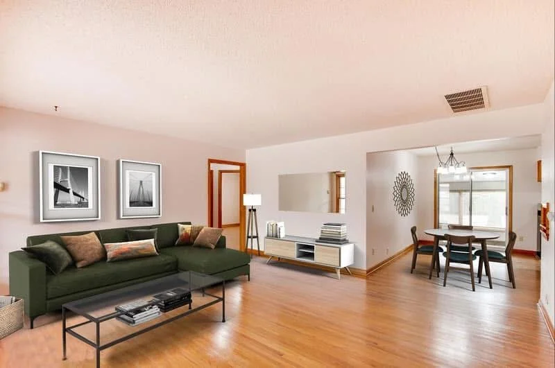 Living room with green sofa, wooden floor, wall art, white media console, round dining table with chairs, and a doorway leading outside.