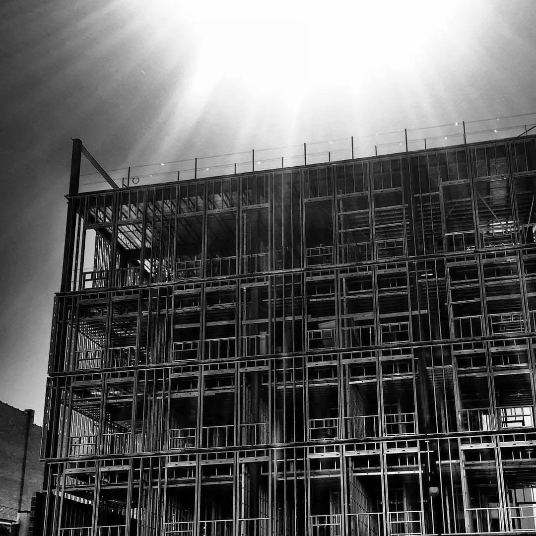 Black and white photo of a multi-story building under construction with exposed metal framework.