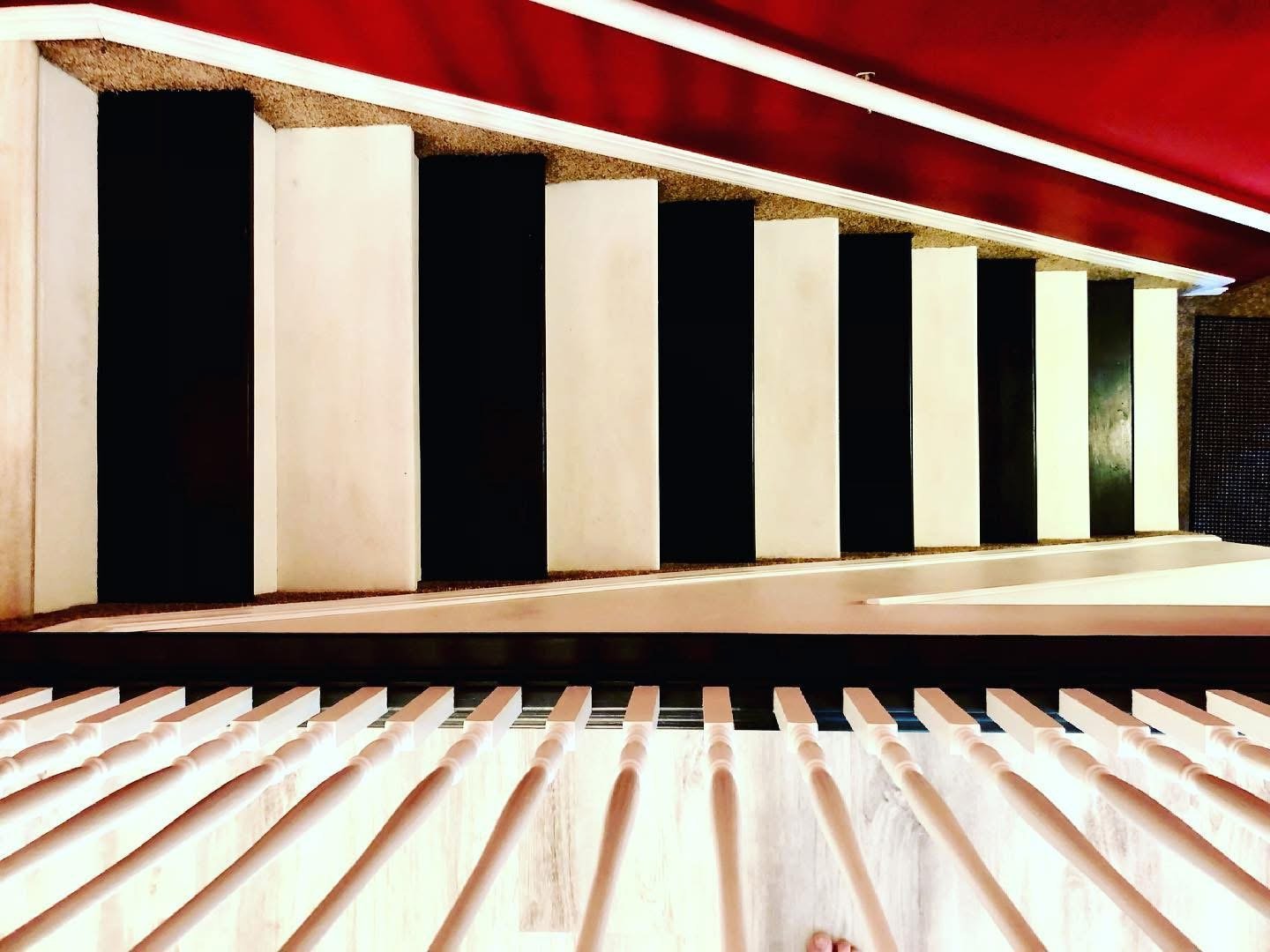 View from above of a modern piano keyboard and part of the interior of a room with red ceiling and black and white acoustic panels.