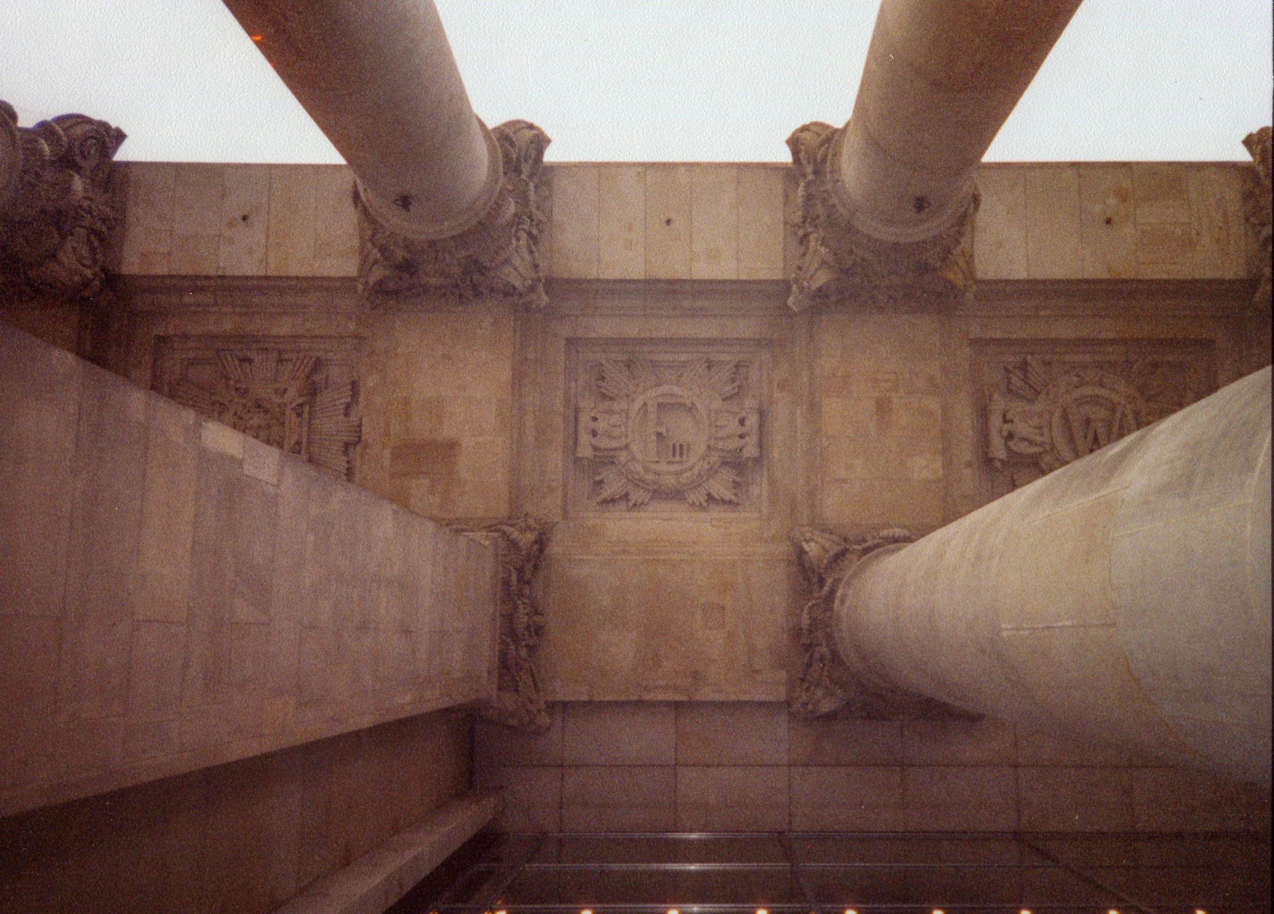Looking up at a stone ceiling with ornate carved columns and a crest or emblem in the center.