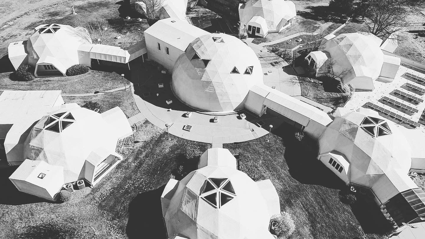 Aerial view of dome-shaped buildings with geometric design, surrounded by pathways, grass, and parking lot, in black and white.