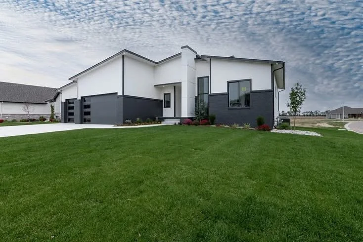 Modern white and gray house with a manicured green lawn and a cloudy sky.