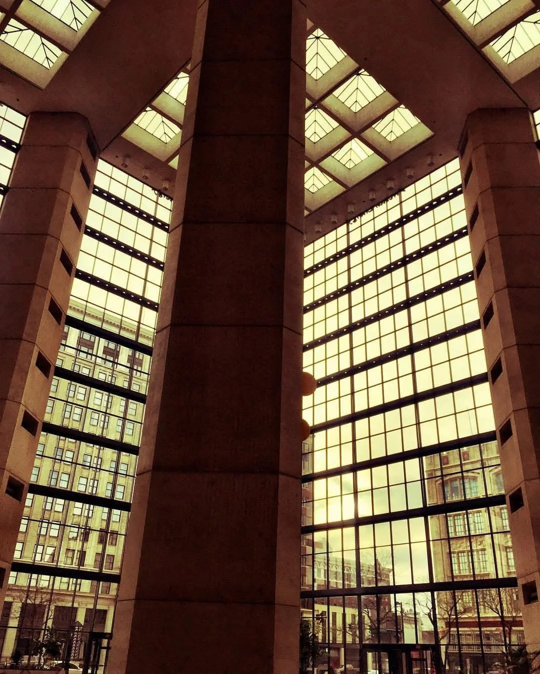 Interior view of a modern building with large glass windows and a high ceiling, showing the cityscape outside.