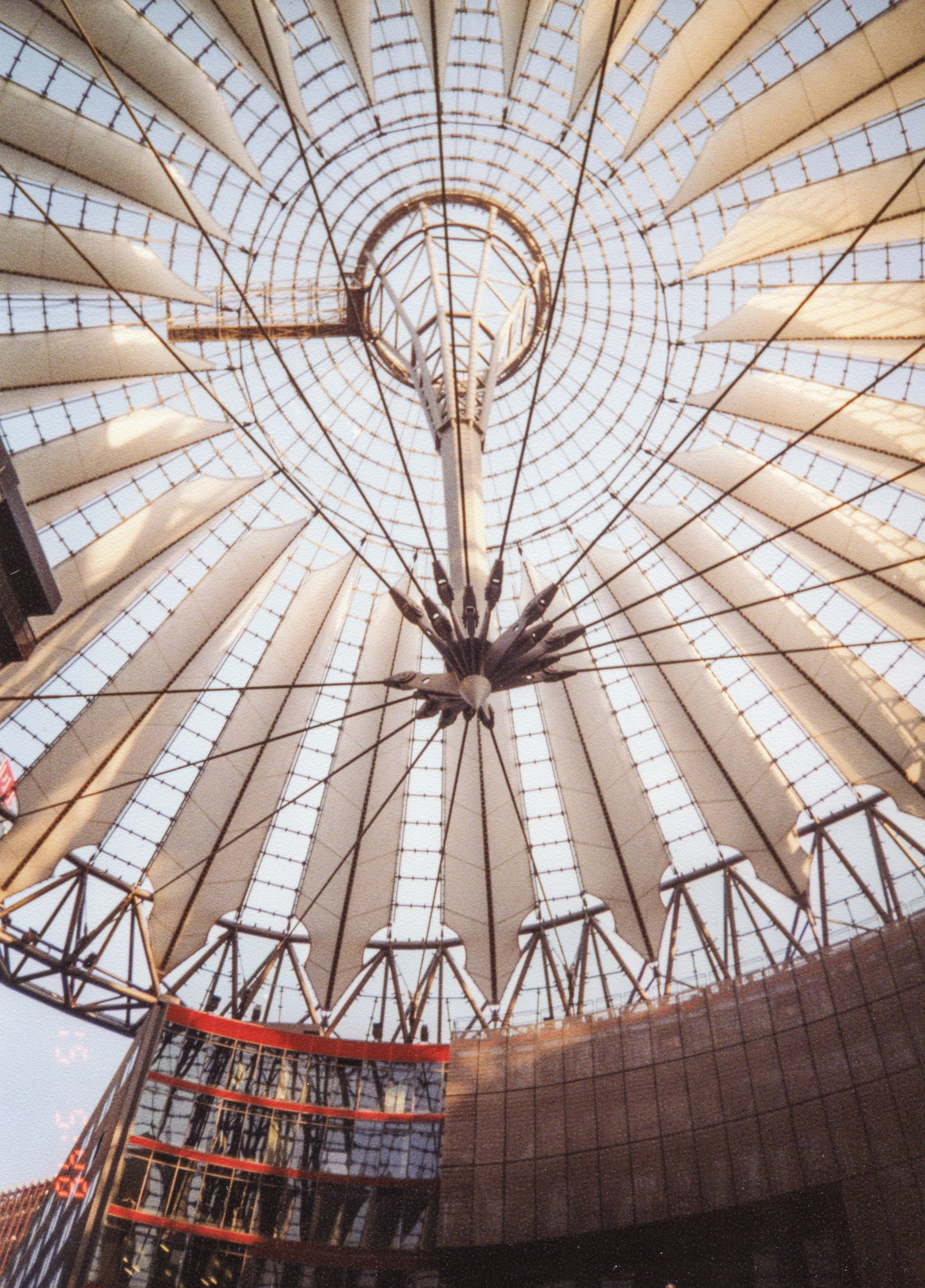 Looking up at a large, circular glass and metal dome ceiling with a central chandelier hanging from the middle.