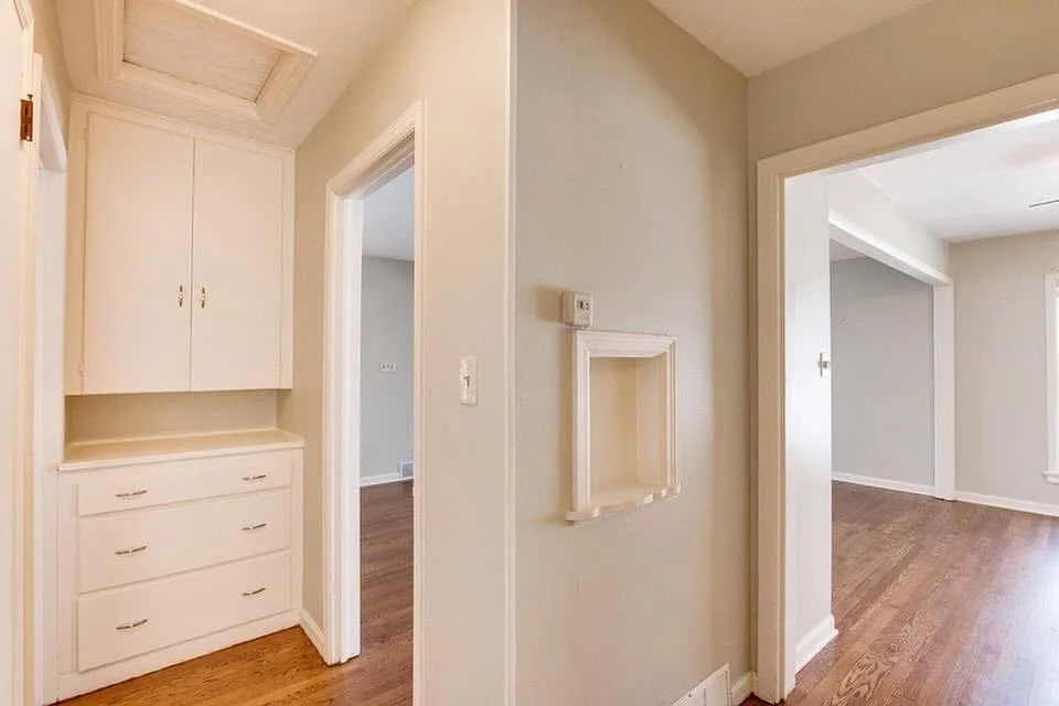 Interior view of a home with beige walls, wooden floors, and white trim, featuring doorways leading to other rooms and built-in white cabinetry.