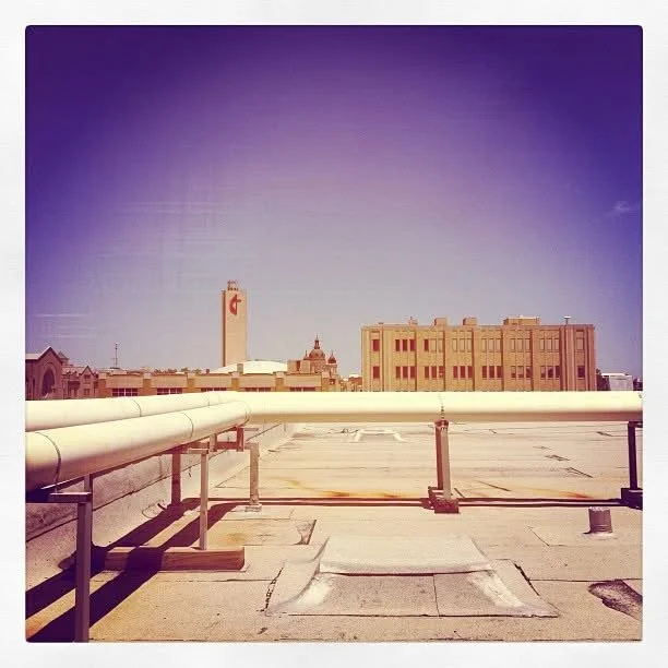View from a rooftop showing a cityscape with buildings and a tower in the distance under a clear purple sky.