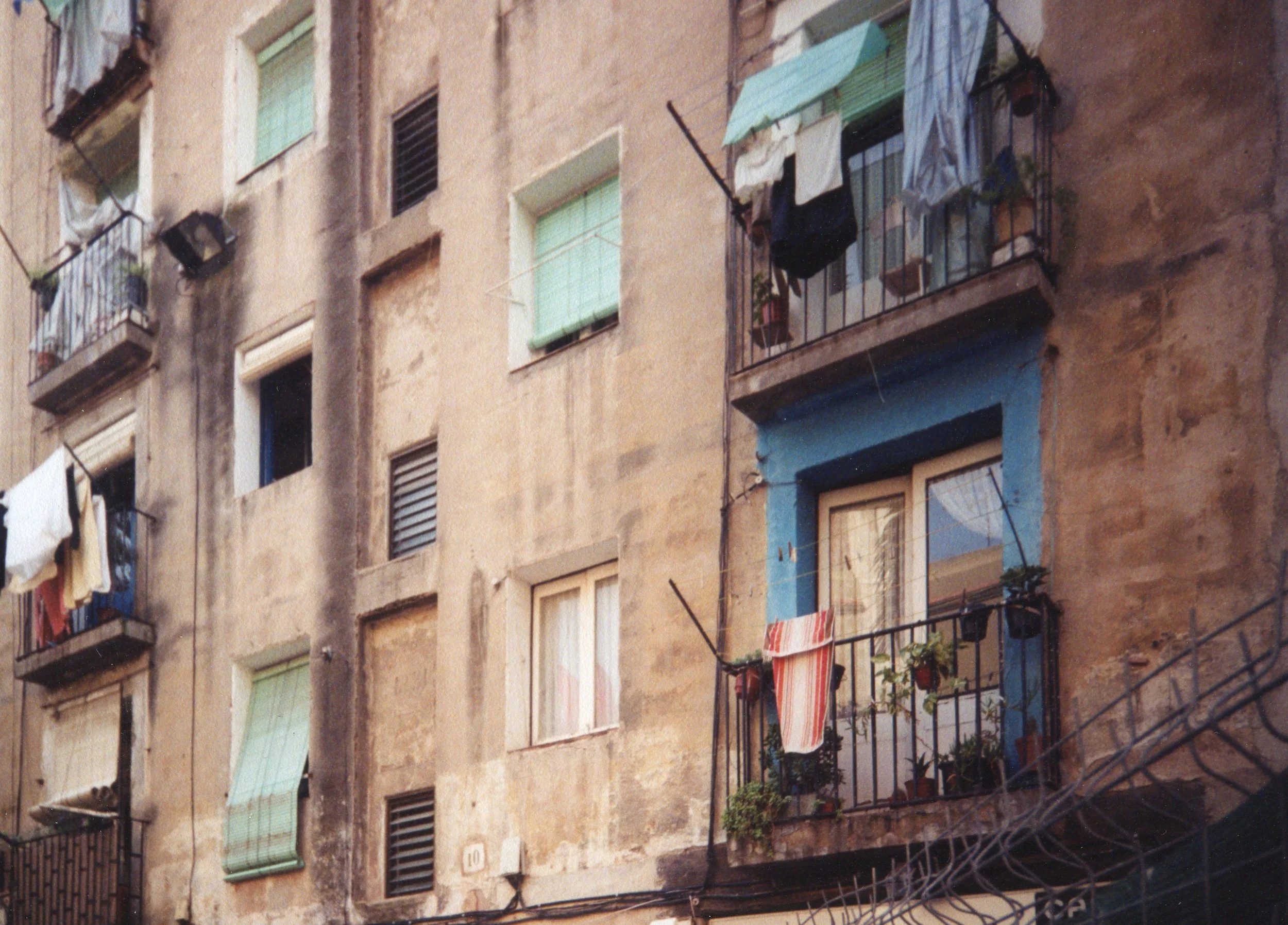A close-up of an old apartment building facade with colorful balconies, windows, and hanging laundry.