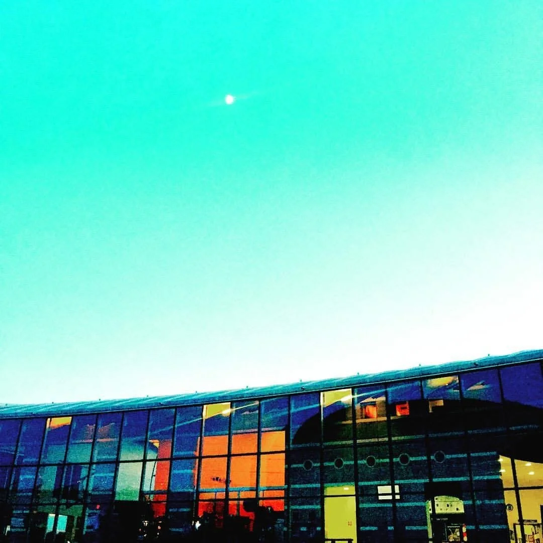 Modern glass building with colorful reflections and a clear greenish sky overhead.
