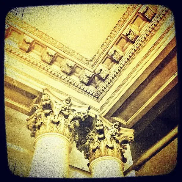 Close-up of ornate architectural details with Corinthian columns, intricate gold carvings, and decorative molding on a ceiling.